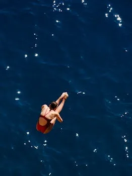Aerial shot of a female diver in red swimwear diving into a deep blue ocean, showcasing freedom and skill.