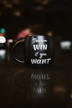 Black mug with inspirational quote 'You can win if you want' reflected on a dark surface, creating a motivational ambiance.